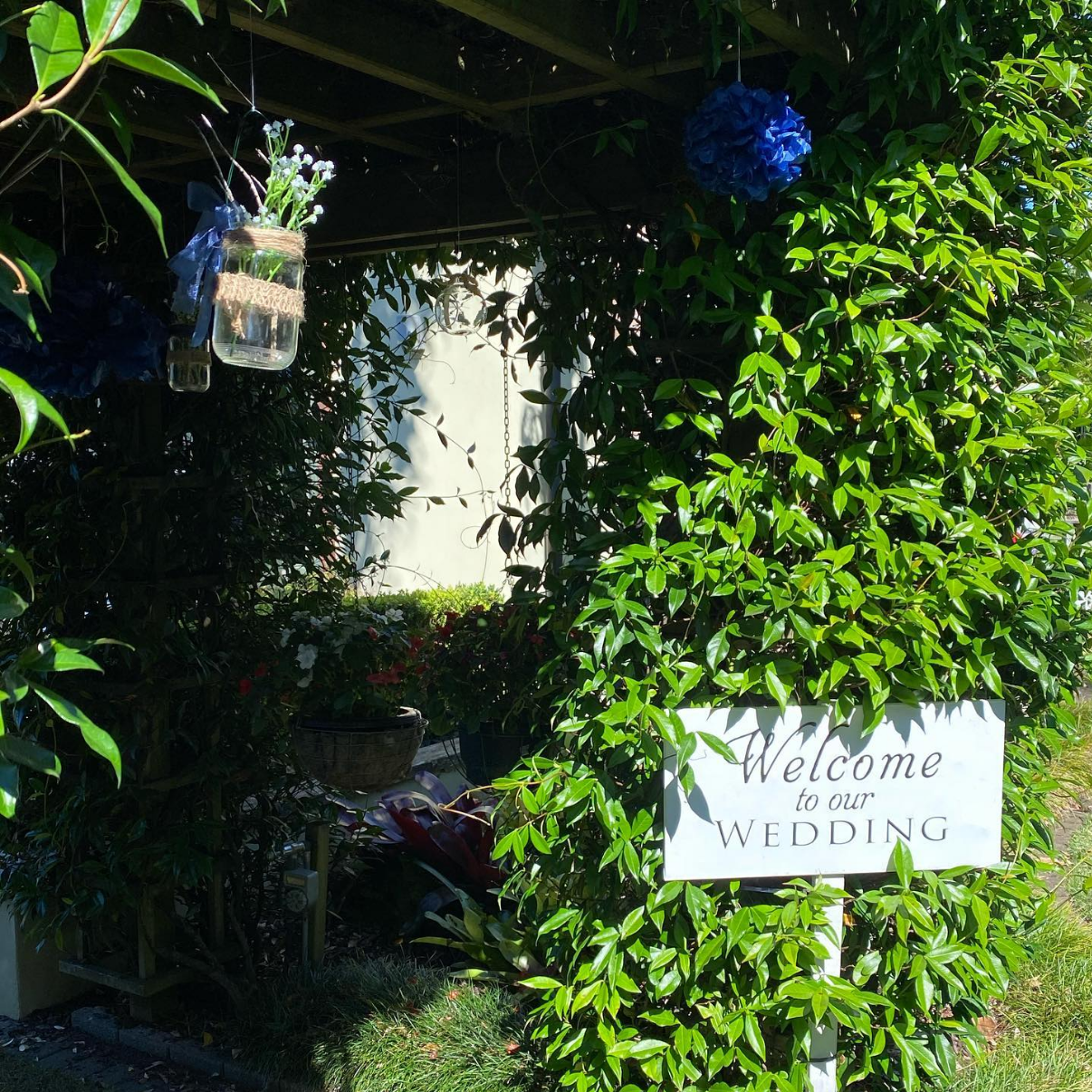 Wedding welcome sign framed by lush greenery and hanging floral jars